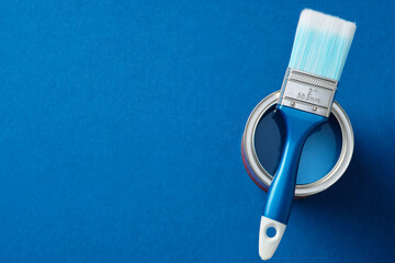 Blue paintbrush resting on an open can of blue paint against a blue background. DIY, home improvement, renovation concept