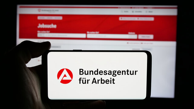 Stuttgart, Germany - 03-07-2025: Person holding cellphone with logo of German federal agency Bundesagentur f&uuml;r Arbeit on screen in front of webpage. Focus on phone display.