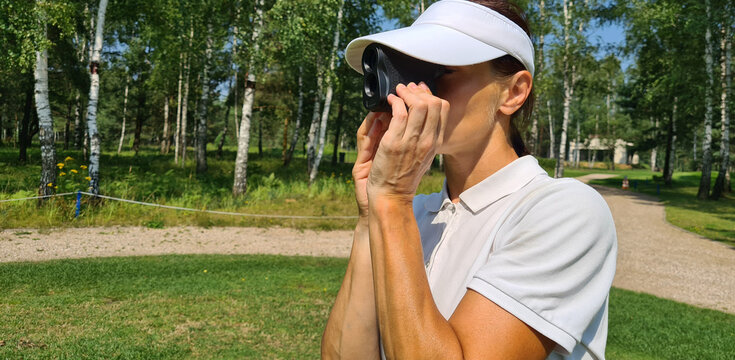 Woman golfer looks into rangefinder to measure distance
