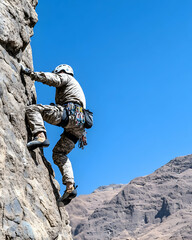 Climber ascends steep rock face against clear blue sky and distant mountains