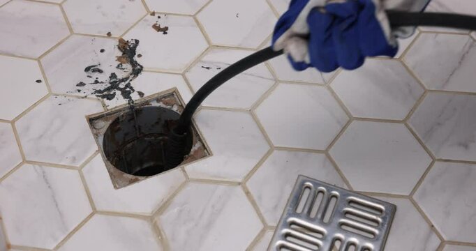 plumber unclogging blocked shower drain with hydro jetting at home bathroom. sewer cleaning service