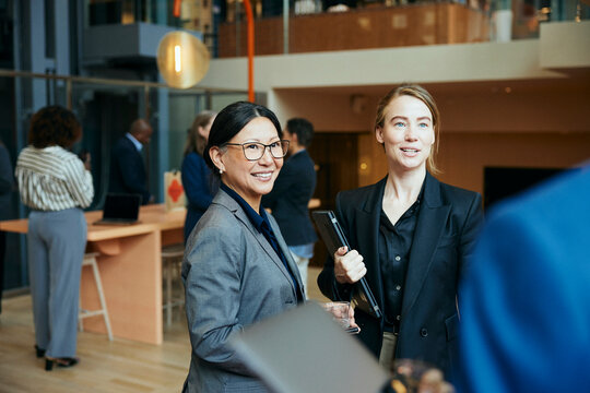 Aff&auml;rskvinnor st&aring;r i lobby av kontorsbyggnad och pratar med kollegor