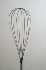 Metal whisk for whipping food on light gray background