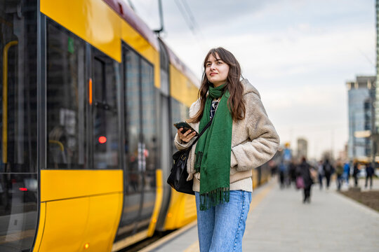 Young woman using mobile phone at the tram stop in the city
