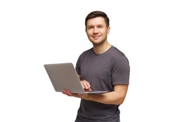 Young man smiling while holding a laptop and standing against a white background in a casual setting