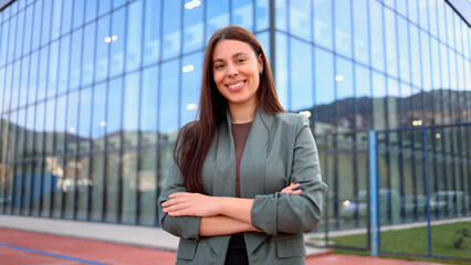 Fototapeta premium Smiling businesswoman posing with folded arms in front of modern office building