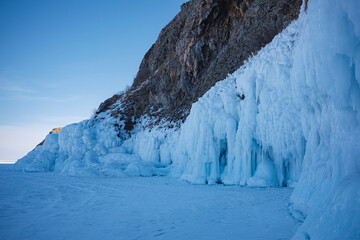 A stunning, towering cliff blanketed in ice and snow, with a majestic mountain standing prominently...
