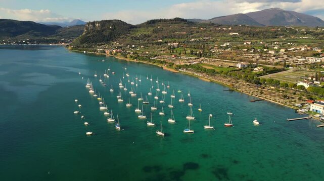 aerial drone scenic video of sailing boats in raws in harbour, coastal village with red roofs at Italian Garda lake in sunny day