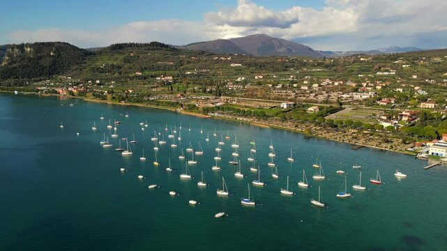 aerial drone scenic video of sailing boats in raws in harbour, coastal village with red roofs at Italian Garda lake in sunny day