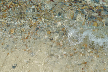 The rocks are under shallow water, so clear that you can see through them. Texture stone pebbles seen through transparent clear waters of the sea background