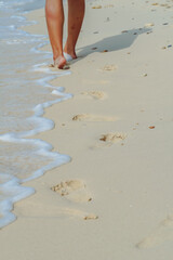 Footsteps leading towards sea at beach. Sand, footprints, pacific ocean surf, tropical beach. Young woman walking over a beach and leaving her footprints on the sand