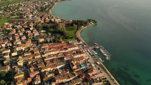 drone above epic video of harbour with boats in Italian Bardolino at Lake Garda with red piled roofs and clear transparent blue water 