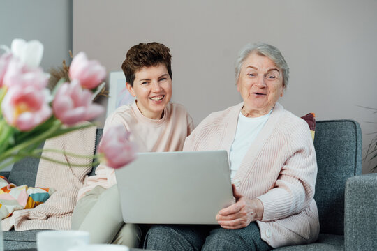 A young woman explaining her senior mother or grandma how to use laptop. Retired lady discovering technology for reading news, chatting with family, watching video, online consulting with doctor.
