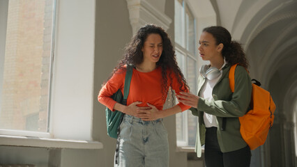 Two students girl Hispanic women Latina female friends in university college walking talking woman feeling stomach ache menstrual pain period painful cramp abdominal health problem medicine gastric