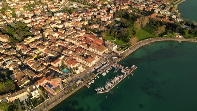 drone above epic video of harbour with boats in Italian Bardolino at Lake Garda with red piled roofs and clear transparent blue water 
