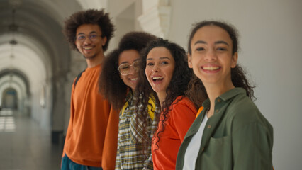 Group happy diversity students in university corridor talking smiling laughing four multiracial friends in college African American man guy with Arabian Hispanic women girls looking to camera positive