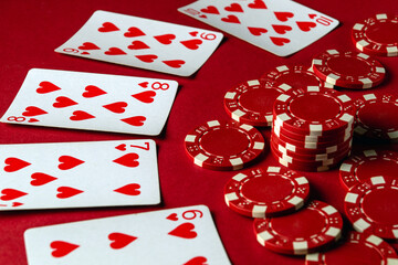 A group of straight flush playing cards and poker chips are arranged on a red table, creating an...