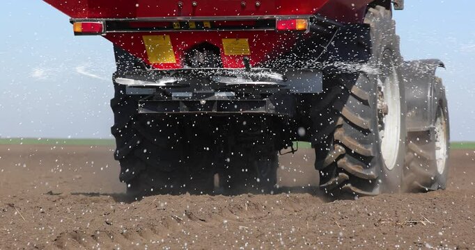 Farmer with agricultural machinery fertilizing agricultural field in spring time, slow motion. Spreading mineral fertilizer, low angle shot