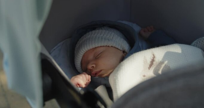 Close-up portrait of a newborn baby boy in a hat sleeping in a stroller covered with blanket.