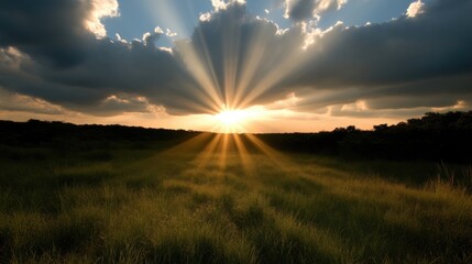 Sunset over a grassy field with dramatic clouds.  Sunlight rays bursting through dark clouds