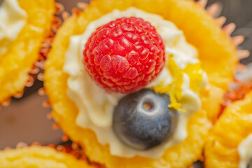Delicious golden cupcakes topped with whipped cream, fresh raspberries, and blueberries in vibrant paper liners. Perfectly detailed with bright colors and soft textures.