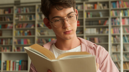 Teenage guy concentrated preparing for exams homework interested in reading book in books store library in high school college studying learning Caucasian man male student education read literature