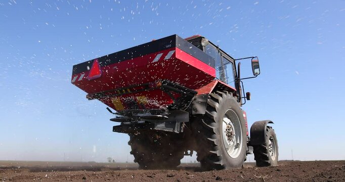 Farmer with agricultural machinery fertilizing agricultural field in spring time, slow motion. Spreading mineral fertilizer, low angle shot