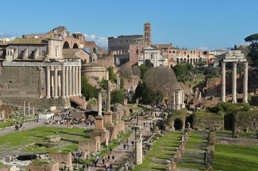 Naklejka premium Majestic architecture fills the landscape of Rome, featuring the famous Colosseum and historical structures. Visitors admire these ancient sites on a sunny day.