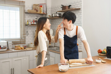 Playful young couple smiling and teasing each other while preparing dough together in bright modern...