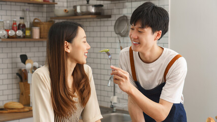 Young couple sharing fruit in modern kitchen while cooking together in playful and romantic atmosphere