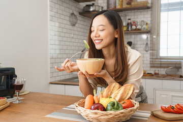 Beautiful young woman enjoying fresh salad with joyful smile in cozy kitchen filled with healthy ingredients