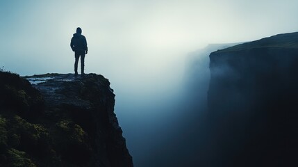 Man Standing on Cliff Edge Surrounded by Mist and Fog in Dramatic Landscape at Dawn or Dusk