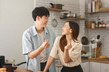 Happy couple showing Korean finger heart symbol while cooking together in cozy kitchen