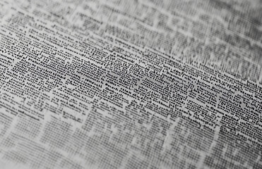 A close up view of a newspaper filled with dense text and small print in black and white tones 