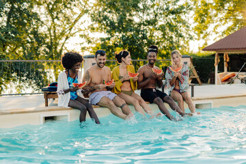 Happy friends eating watermelon and splashing in a pool during summer vacation