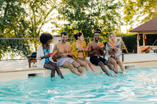 Happy friends eating watermelon and splashing in a pool during summer vacation