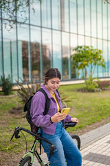Fototapeta premium Young woman texting with one hand while leaning on her bicycle, digital lifestyle