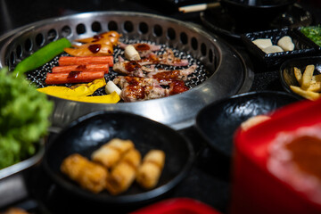 A woman's hand holding chopsticks with Full set of beef and pork ready for grill on stove serve with vegetable, soup and rice and side dish, barbecue style.
