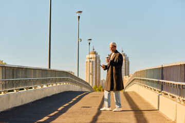 Stylish man with tattoos enjoying a sunny day while sipping coffee on a city bridge