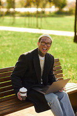 Obraz premium Stylish young man enjoying a sunny afternoon while working on his laptop in the park