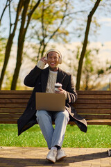 Fototapeta premium Stylish young man with tattoos lounges in a sunny park enjoying music and coffee