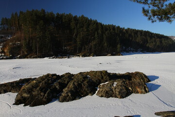 Winter landscape with snow-covered forest and river in the Altai mountains. Manzherok is a rural...