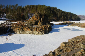 Winter landscape with snow-covered forest and river in the Altai mountains. Manzherok is a rural...