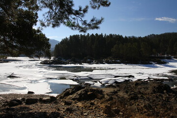 Winter landscape with snow-covered forest and river in the Altai mountains. Manzherok is a rural...