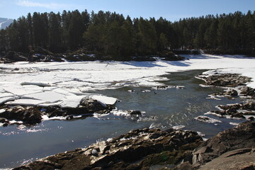 Winter landscape with snow-covered forest and river in the Altai mountains. Manzherok is a rural...