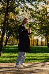 Stylish young man with tattoos enjoying a sunny day in a vibrant park while sipping coffee
