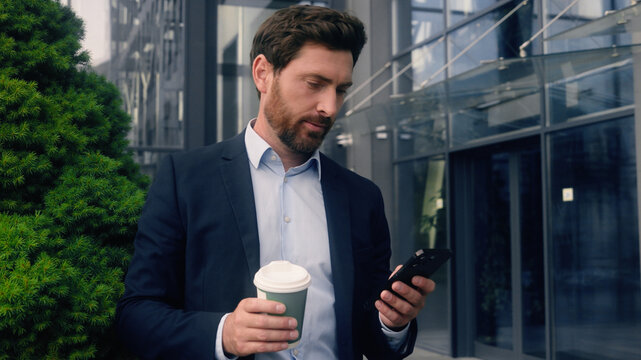 Male manager in city near office drinking coffee looking away relaxed thinking dreaming smiling calm look check time with mobile phone Caucasian man business guy employer businessman run late to work