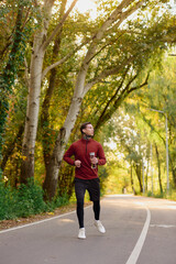 Fototapeta premium Stylish young man with tattoos jogs through a scenic park during a sunlit autumn afternoon