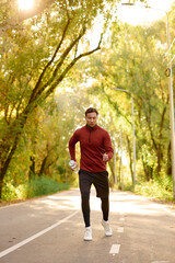 Stylish young man jogging in a sunlit pathway surrounded by vibrant autumn trees