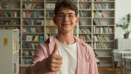 Teenage guy in books store library in high school college looking at camera smiling positive...